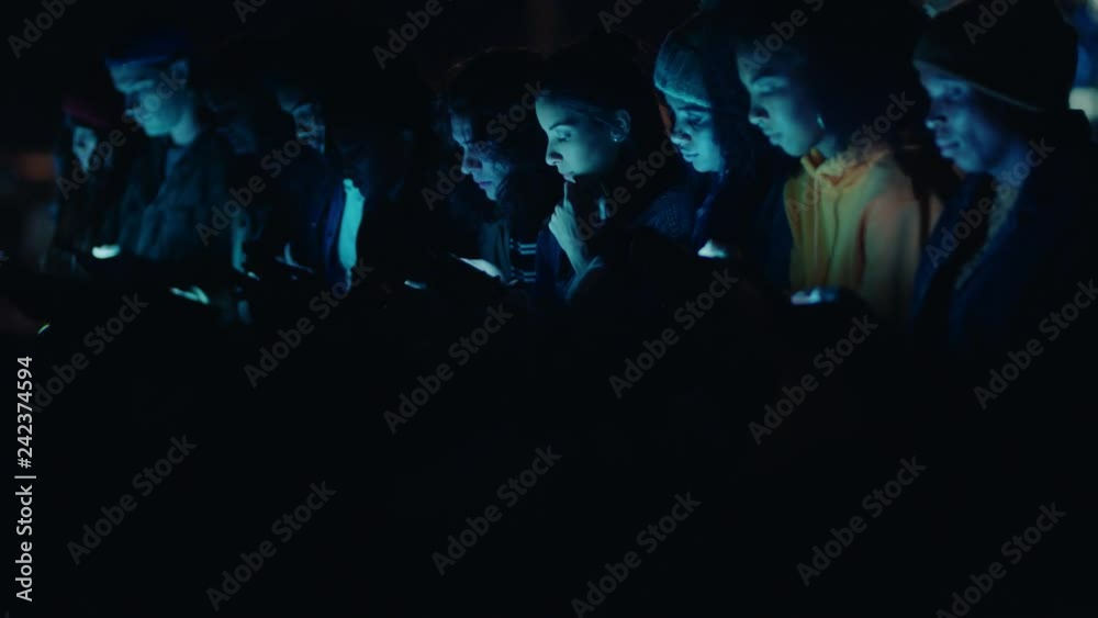 group of friends using smartphone mobile technology hanging out on rooftop at night enjoying weekend sharing social media messages addiction concept