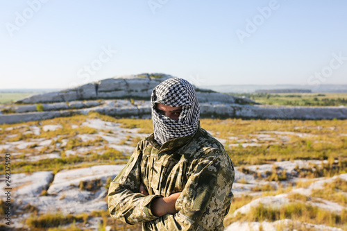 Soldier is standing in the camouflage uniform and checkered keffiyeh shemagh bandana. Terrorist is outdoors in the abandoned deserted place. No war concept. photo