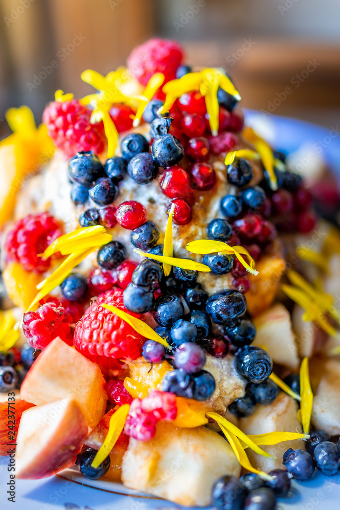 Macro vertical closeup of colorful bowl of ice cream topped with vibrant blue blueberries bilberries, calendula yellow flower petals dessert