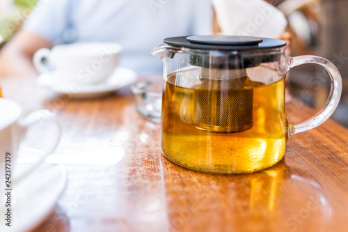 Closeup of white cups on plates and green or herbal oolong tea in breakfast brunch outdoor cafe restaurant outside wooden table with sunny teapot or pot