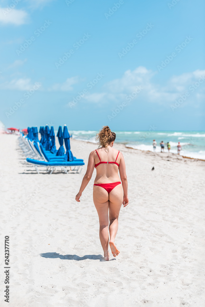 Young woman in red swimsuit bikini thong on beach during sunny day