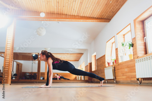 Sporty beautiful young woman practicing yoga, working out, doing easy alternative to Chaturanga Dandasana, half push-up, Eight-Limbed or Caterpillar pose, Ashtanga Namaskara, studio. photo