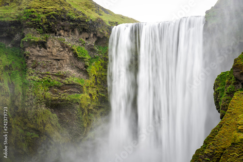 Skogafoss, Iceland dramatic waterfall on cliff with green grass moss and nobody in summer with smooth long exposure motion of water, and closeup of stream