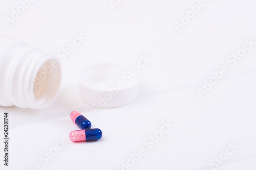 Open plastic jar and two dark blue and pink transparent capsules with micro-granules inside on white background