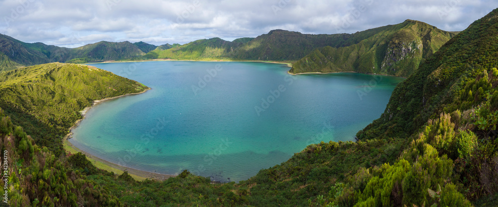 Panoramic landscape with beautiful blue crater lake Lagoa do Fogo from top of the hill on hiking trail. Lake of Fire is the highest lake of Sao Miguel island, surrounded by Natural Reserve green