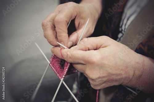 The hands of an elderly woman knit clothes out of wool yarn with knitting needles