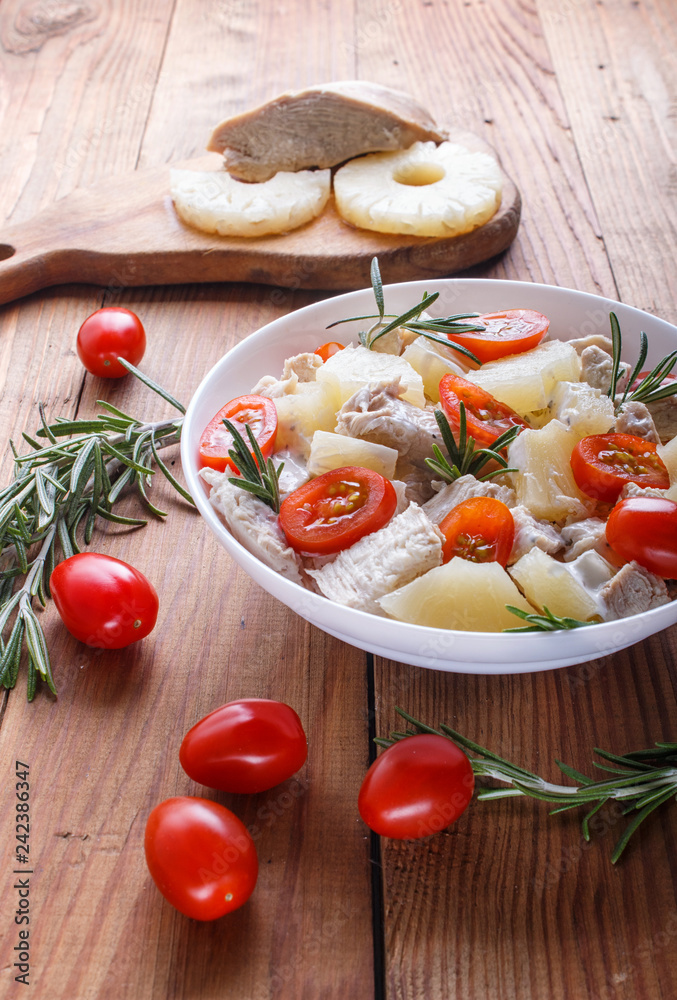 Chicken fillet salad with rosemary, pineapple and cherry tomatoes on brown wooden background.