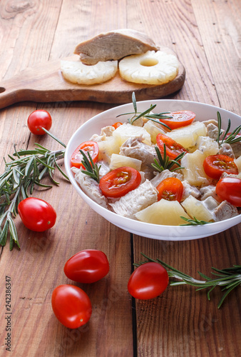 Chicken fillet salad with rosemary, pineapple and cherry tomatoes on brown wooden background.