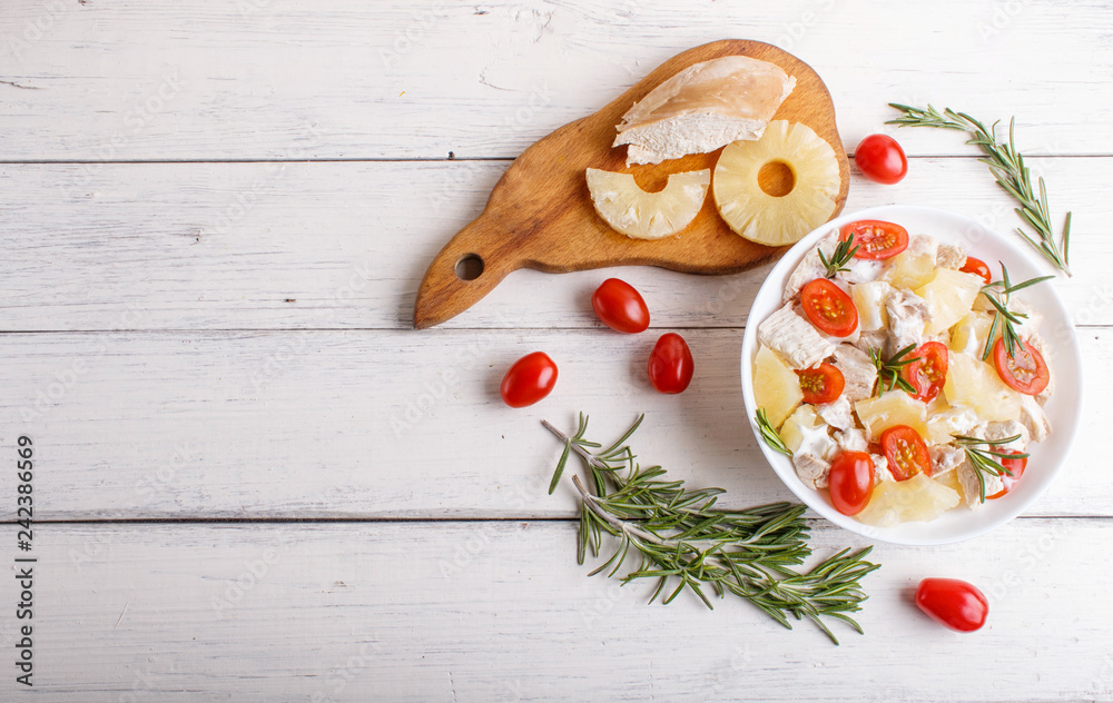 Chicken fillet salad with rosemary, pineapple and cherry tomatoes on white wooden background.