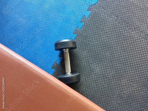 The blue and black rubber gym floor with a dumbell and a bench.