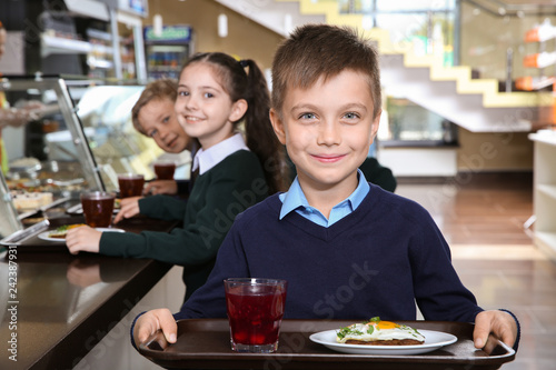 Cute boy holding tray with healthy food in school canteen photo
