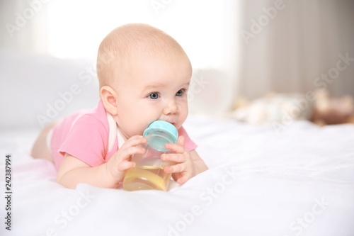 Pretty baby lying with bottle on bed at home. Space for text