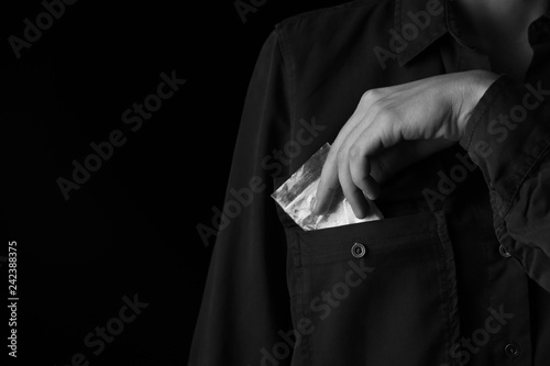 Drug dealer taking bag with cocaine out of pocket on black background, closeup. Space for text