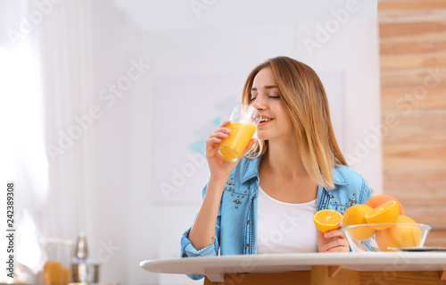Beautiful young woman drinking orange juice at table indoors, space for text. Healthy diet