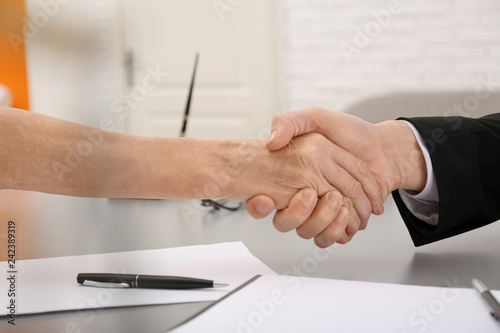 Lawyer shaking hands with client in office, closeup photo