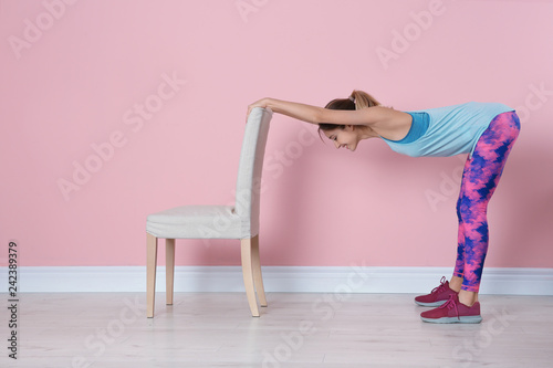 Young woman exercising with chair near color wall. Home fitness