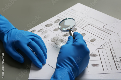 Criminalist exploring fingerprints with magnifying glass at table, closeup