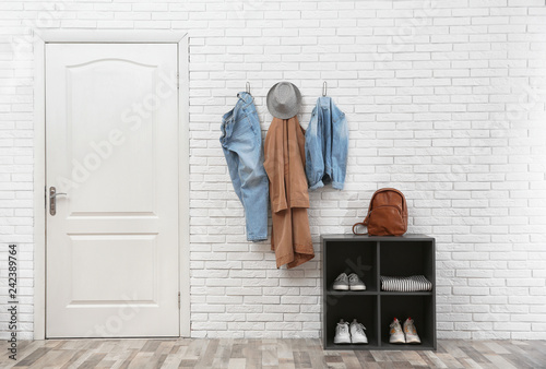 Stylish hallway interior with door, shoe rack and clothes hanging on brick wall