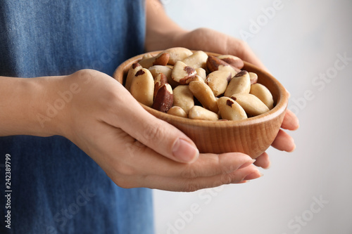 Woman holding bowl with Brazil nuts on grey background, closeup