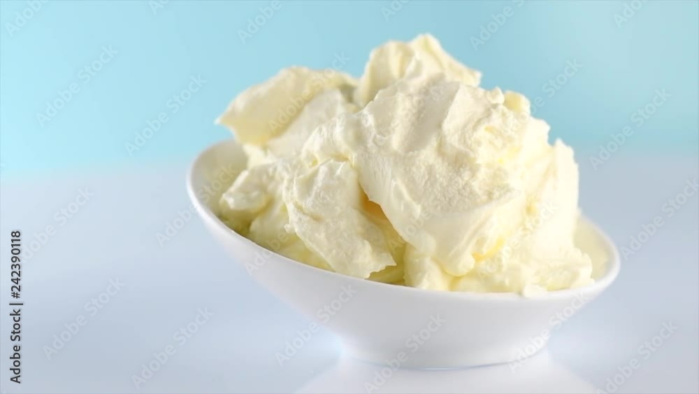 Mascarpone cream cheese closeup. Mascarpone soft milk cream in white bowl rotated on blue background. Homemade ice cream, yoghurt. Slow motion 4K UHD video footage. 3840X2160 Mascarpone cream cheese closeup. Mascarpone soft milk cream in white bowl rotated on blue background. Homemade ice cream, yoghurt. Slow motion 4K UHD video footage. 3840X2160