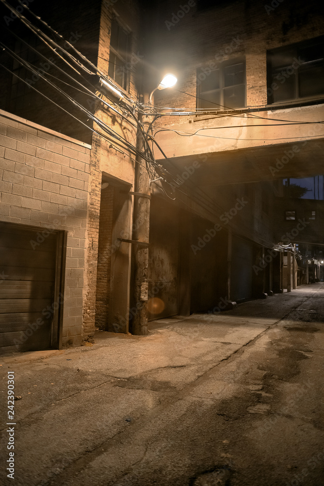 Dark and scary downtown urban city street alley scene with an eerie vintage industrial warehouse factory skyway at night in Chicago