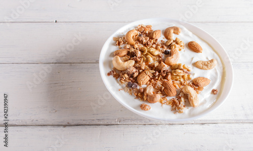 White plate with greek yogurt, granola, almond, cashew, walnuts  on white wooden background.