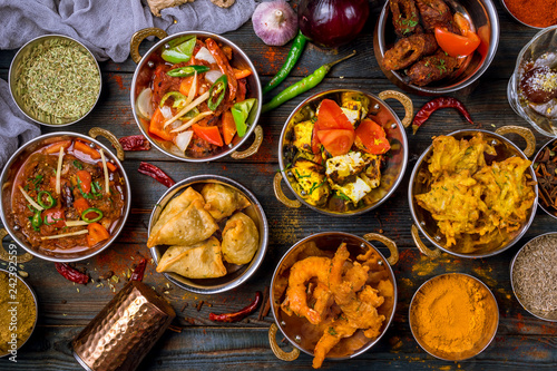Assorted indian food set on wooden background. Dishes and appetisers of indeed cuisine, rice, lentils, paneer, samosa, spices, masala. Bowls and plates with indian food