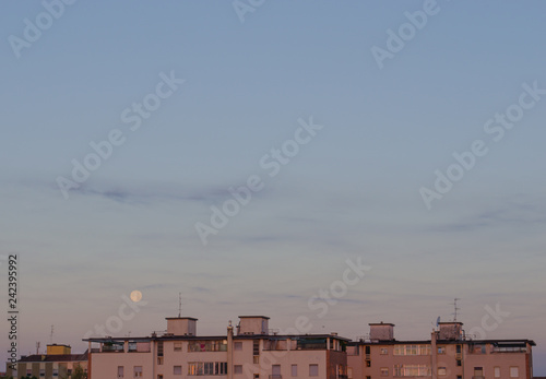 full moon set over the city after sunrise