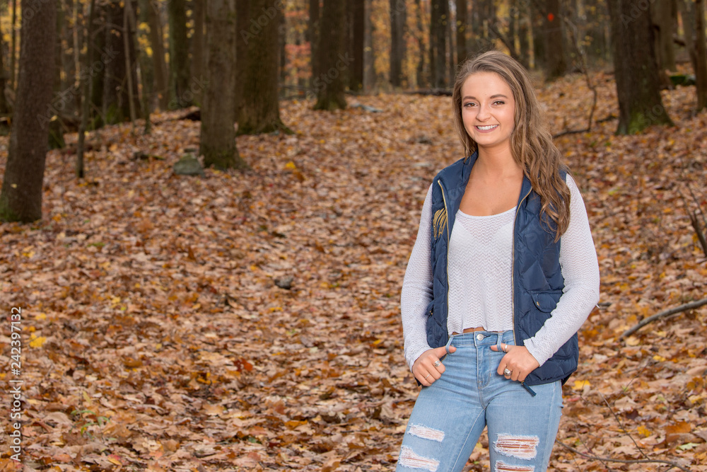 Cute young woman in blue vest and jeans stands in autumn woods Cute young woman in blue vest and jeans stands in autumn woods