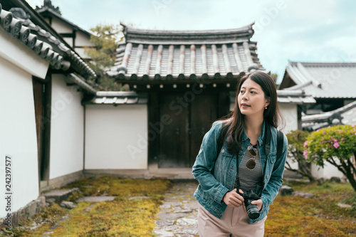 backpacker photographer holding professional slr camera looking around in japanese garden in valley of the temples. girl tourist standing in nature green grass plants trees in byodo in spring. photo