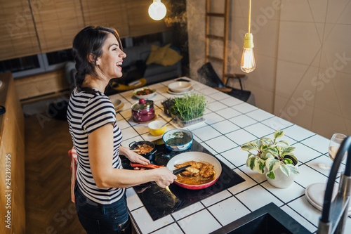 Young woman tasting a healthy meal in home kitchen.Making dinner on kitchen island standing by induction hob.Preparing fresh vegetables,enjoying spice aromas.Eating in.Passion for cooking.Keto diet photo