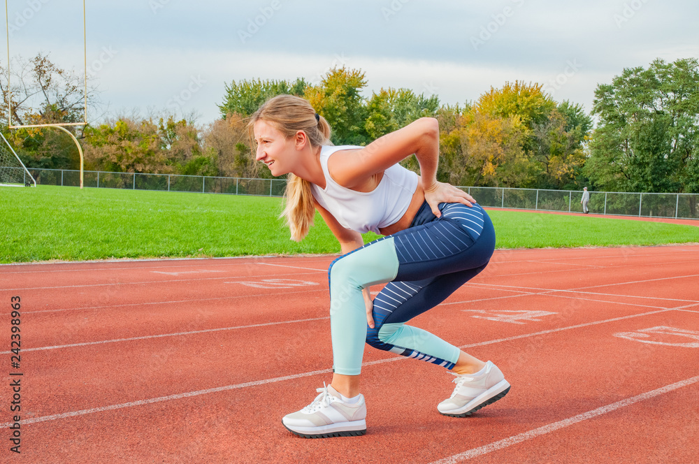 Back pain. Athletic woman on running track touching back with painful injury