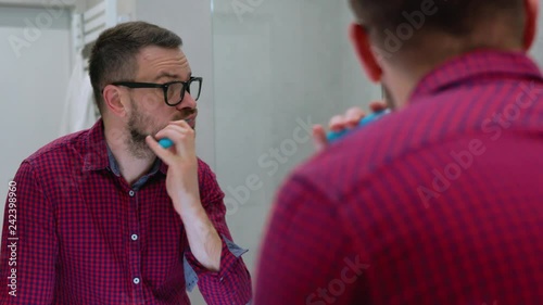 Bearded man brushing his teeth in a bathroom in the morning. Morning hygiene. photo