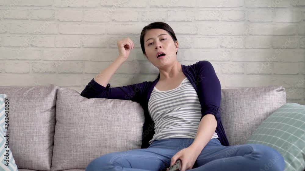 Tired sleeping woman sitting on sofa and yawning indoor living room. young housewife holding television controller keep switching tv program feeling not interested bored. elegant wife sitting relax. Tired sleeping woman sitting on sofa and yawning indoor living room. young housewife holding television controller keep switching tv program feeling not interested bored. elegant wife sitting relax.