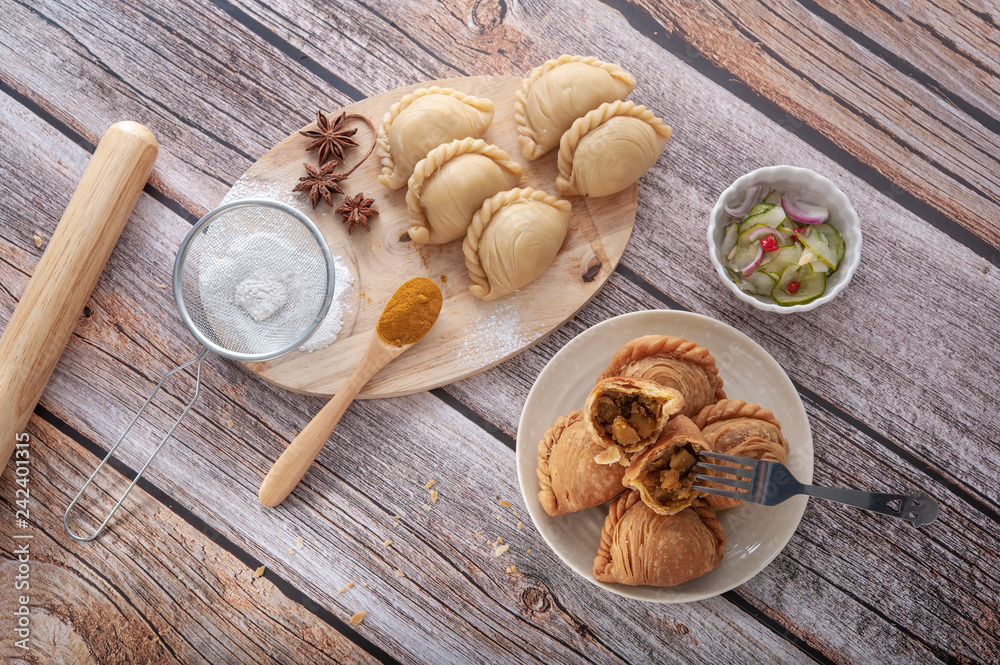Traditional curry puffs stuffed chicken with raw curry puffs on wooden table as background