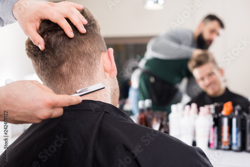 fashionable guy stylist creating haircut for man client at hairdressing salon