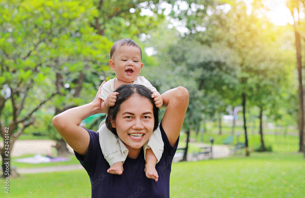 Beautiful young Asian mother with happy baby boy riding on mom's shoulder in the nature park.