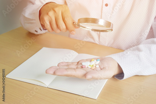 Background in warm light,Asian man wearing shirts holding pills on hand.  Use a magnifying glass to see what kind of medicine. Because the eyes began to have problems.