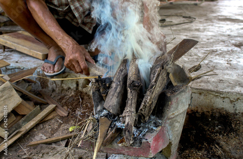 Elderly Asian men put firewood on traditional stove and turn on the fire with the lighter, See smokes coming up on them.