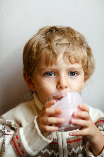 Happy little blond kid boy drinking milk or strawberry milkshake for breakfast or lunch. Healthy eating for children. Happy child in colorful clothes having breakfast