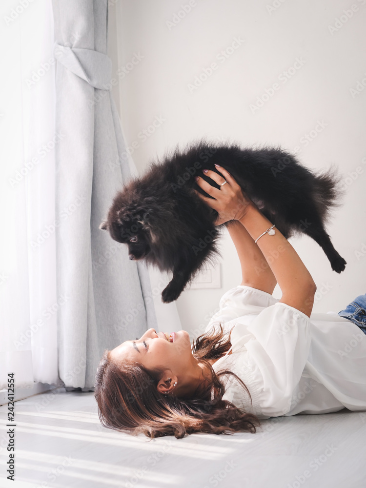Happy Asian woman lying on floor and touching her black dog with window light, lifestyle concept. Happy Asian woman lying on floor and touching her black dog with window light, lifestyle concept.