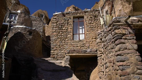 Handheld, medium wide, tilting up, exterior shot of multiple homes built into the rocks at the Kandovan Village.