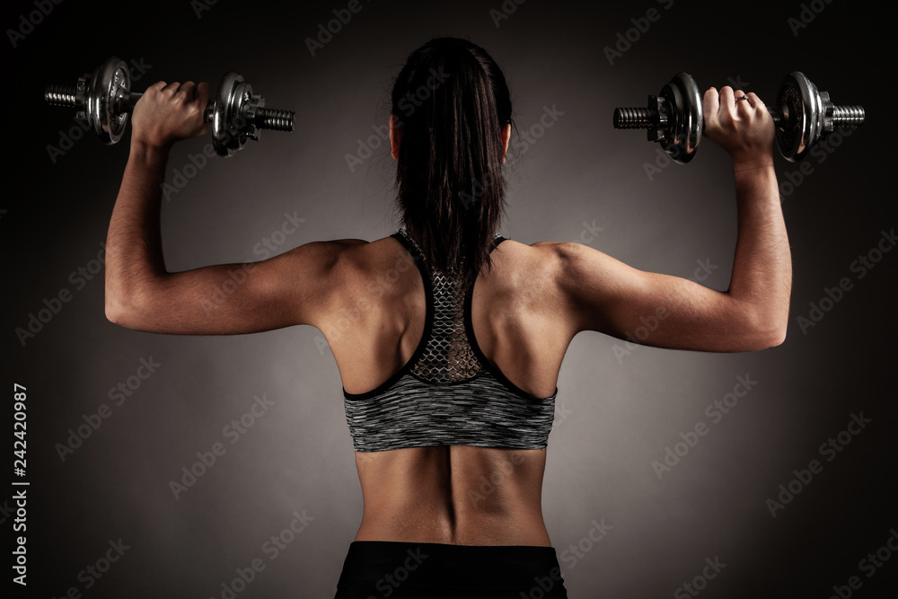 Beautiful young woman workout with dumbbell over gray background in fitness gym club Beautiful young woman workout with dumbbell over gray background in fitness gym club