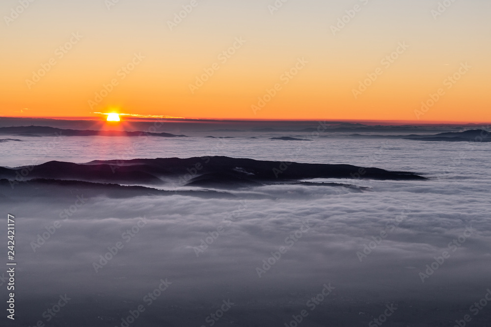 Obraz premium Beautiful sunset over a valley filled by fog with mountains and hills