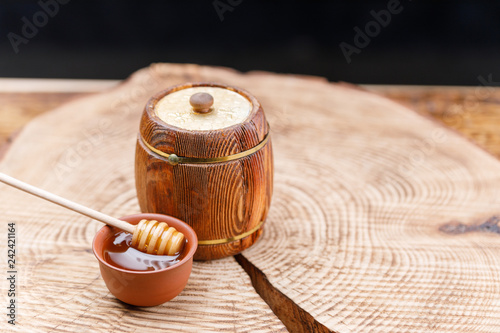 Wooden barrel with fresh honey and a honey spoon in a clay bowl on a textured wooden saw. Barrel.