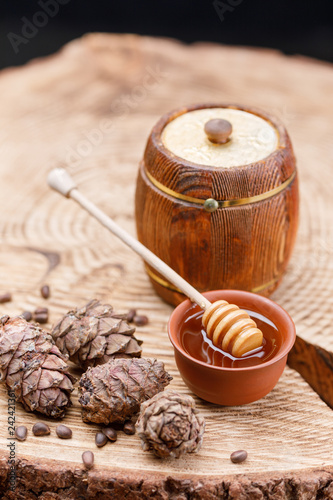 Barrel with honey and honey stick on a wooden background with pine nuts and pine cones. Textured wood products.