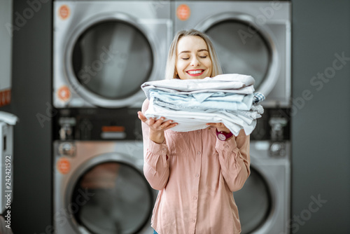 Young woman enjoying clean ironed clothes in the self serviced laundry with dryer machines on the background photo