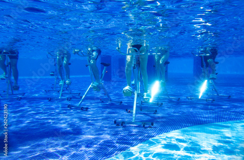 Fitness class doing aqua aerobics on exercise bikes in swimming pool resort hotel