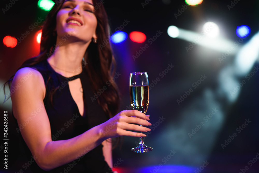 holidays, nightlife, drinks, people and luxury concept - beautiful young woman drinking champagne at party over lights background.