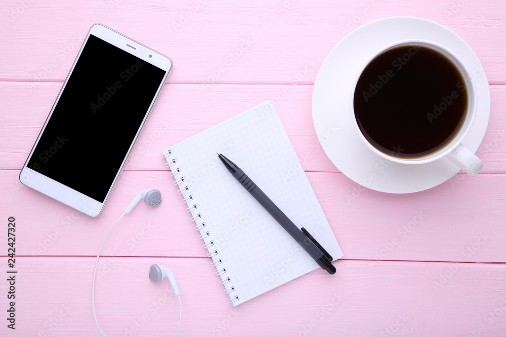 Smart phone with notebook and cup of coffee on pink wooden background Smart phone with notebook and cup of coffee on pink wooden background